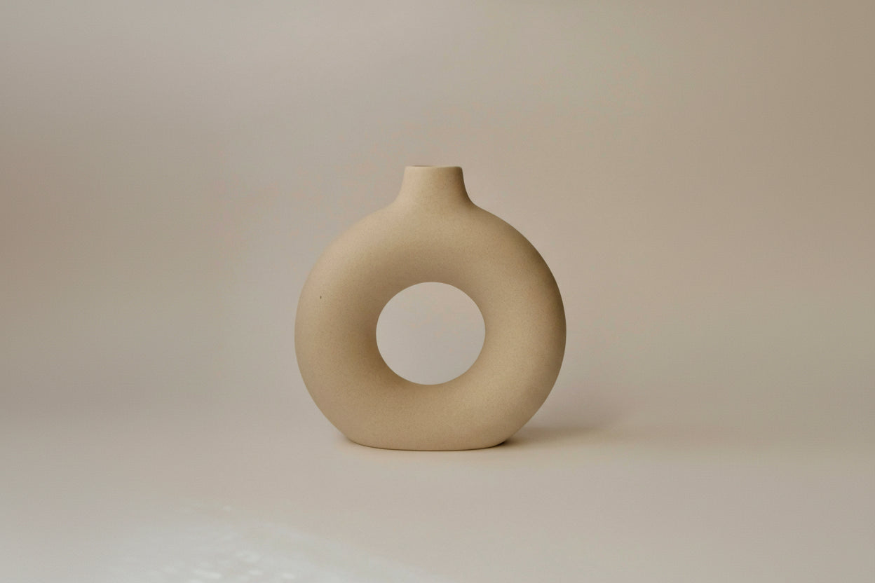 Beige ceramic vase with a circular hole on a beige background