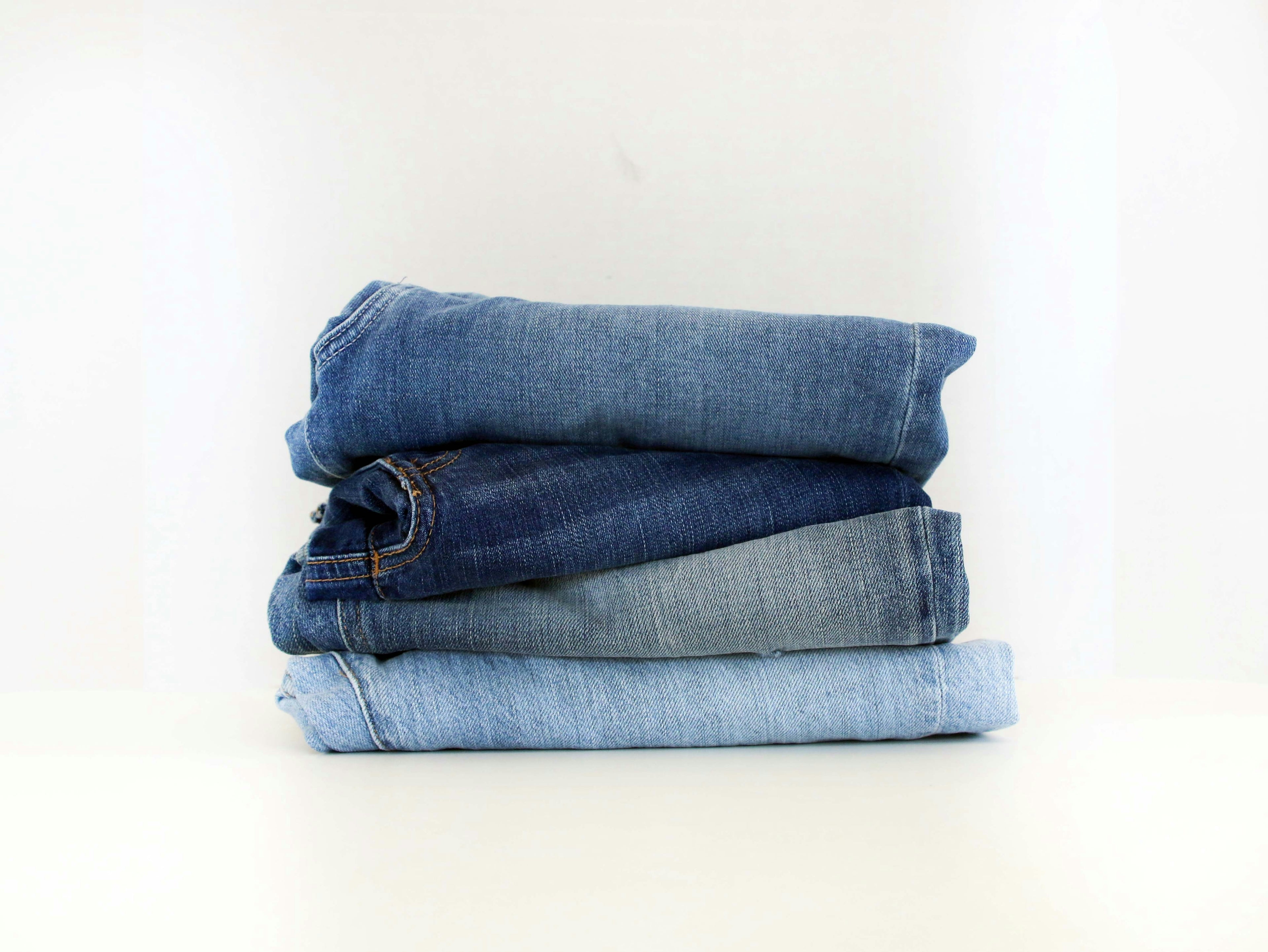 NUADH STUDIO - DENIM DESIGN AND PRODUCTION. Stack of folded blue jeans on a white background